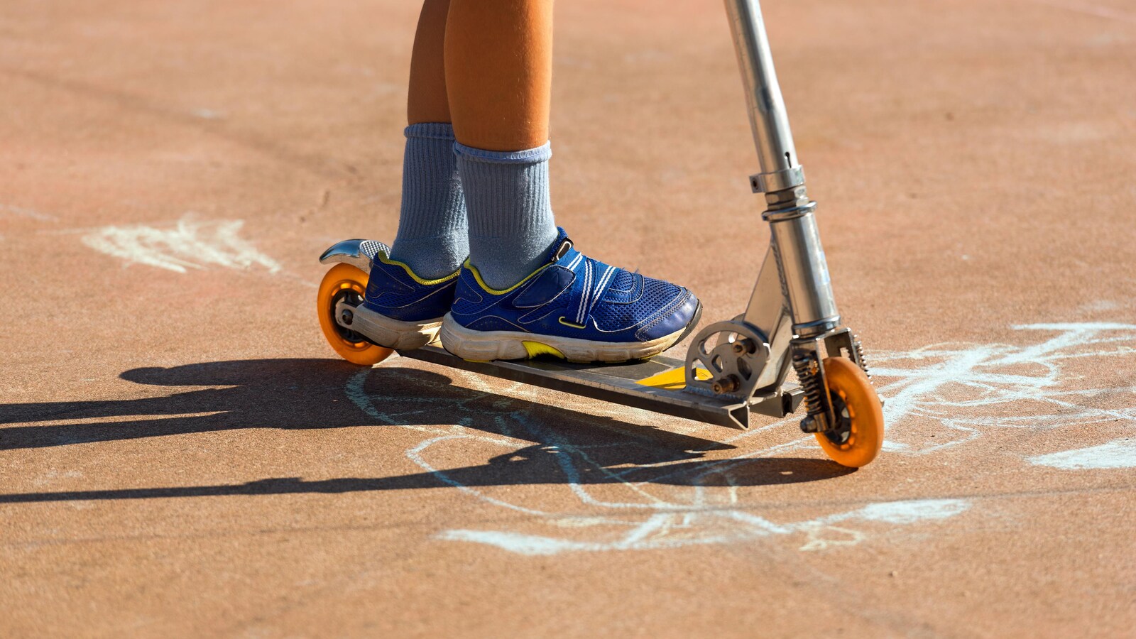 Gros plan sur les chaussures d'un garçon debout sur une trottinette.