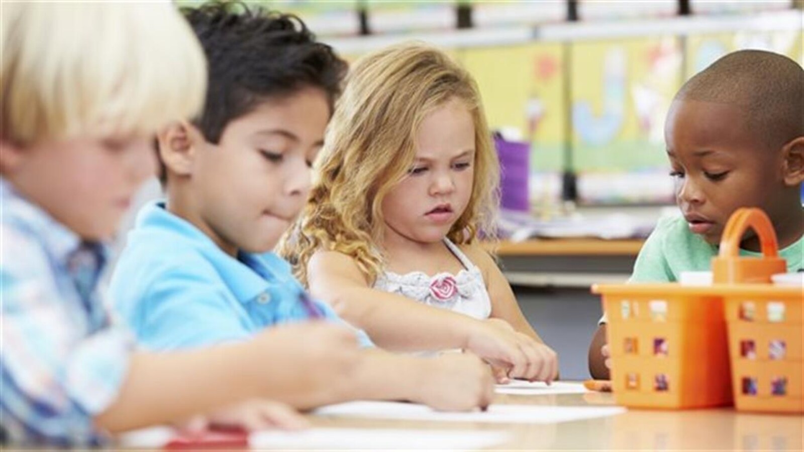 Quatre enfants dessinent à une table dans une garderie.