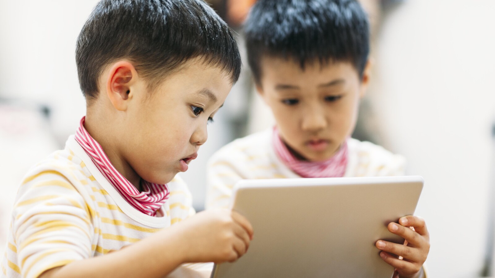 Deux petits garçons regardent une tablette électronique.