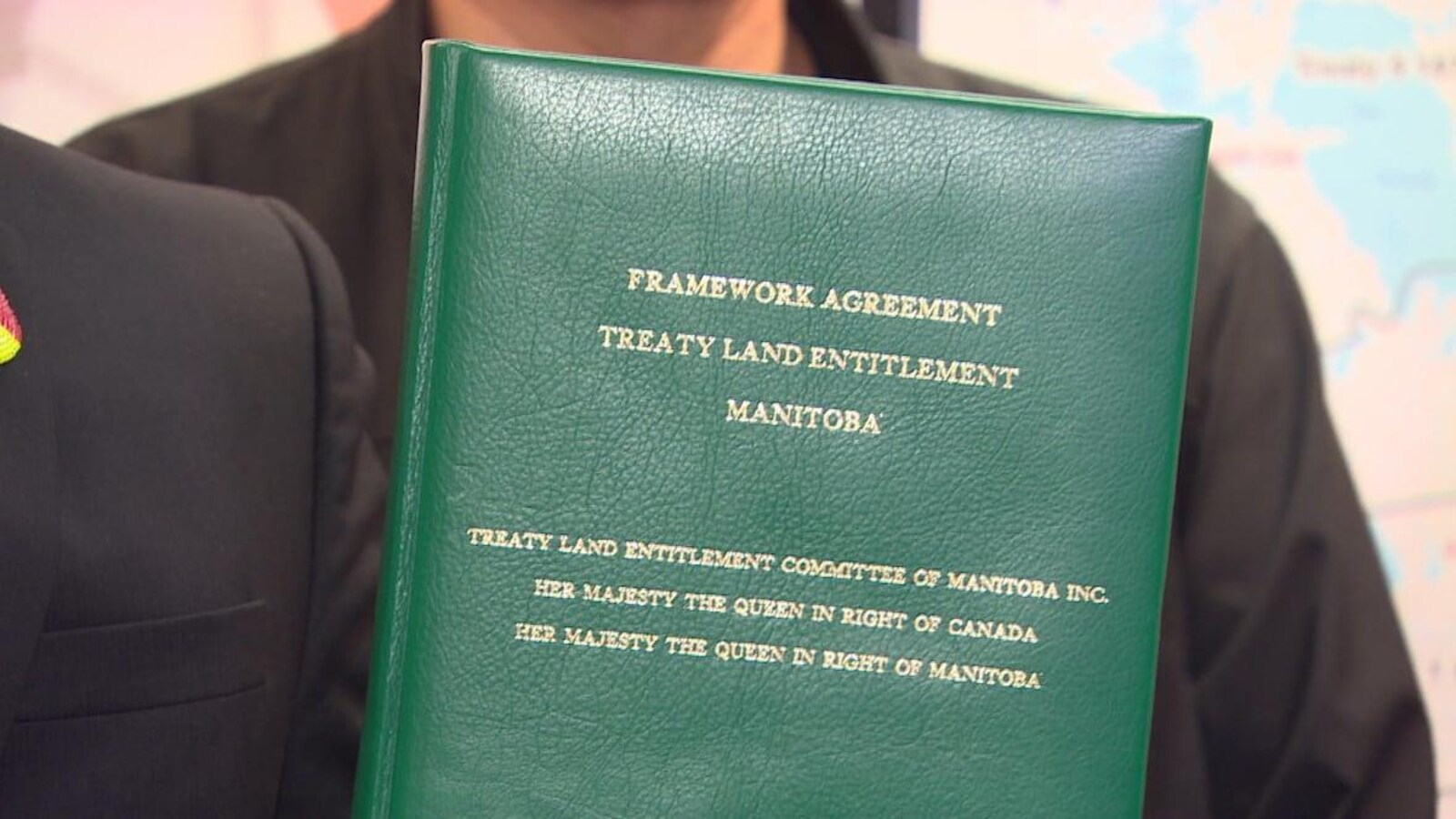 Une personne qu'on ne voit pas, tient un document relié en vert sur lequel on peut lire le titre de l'entente.