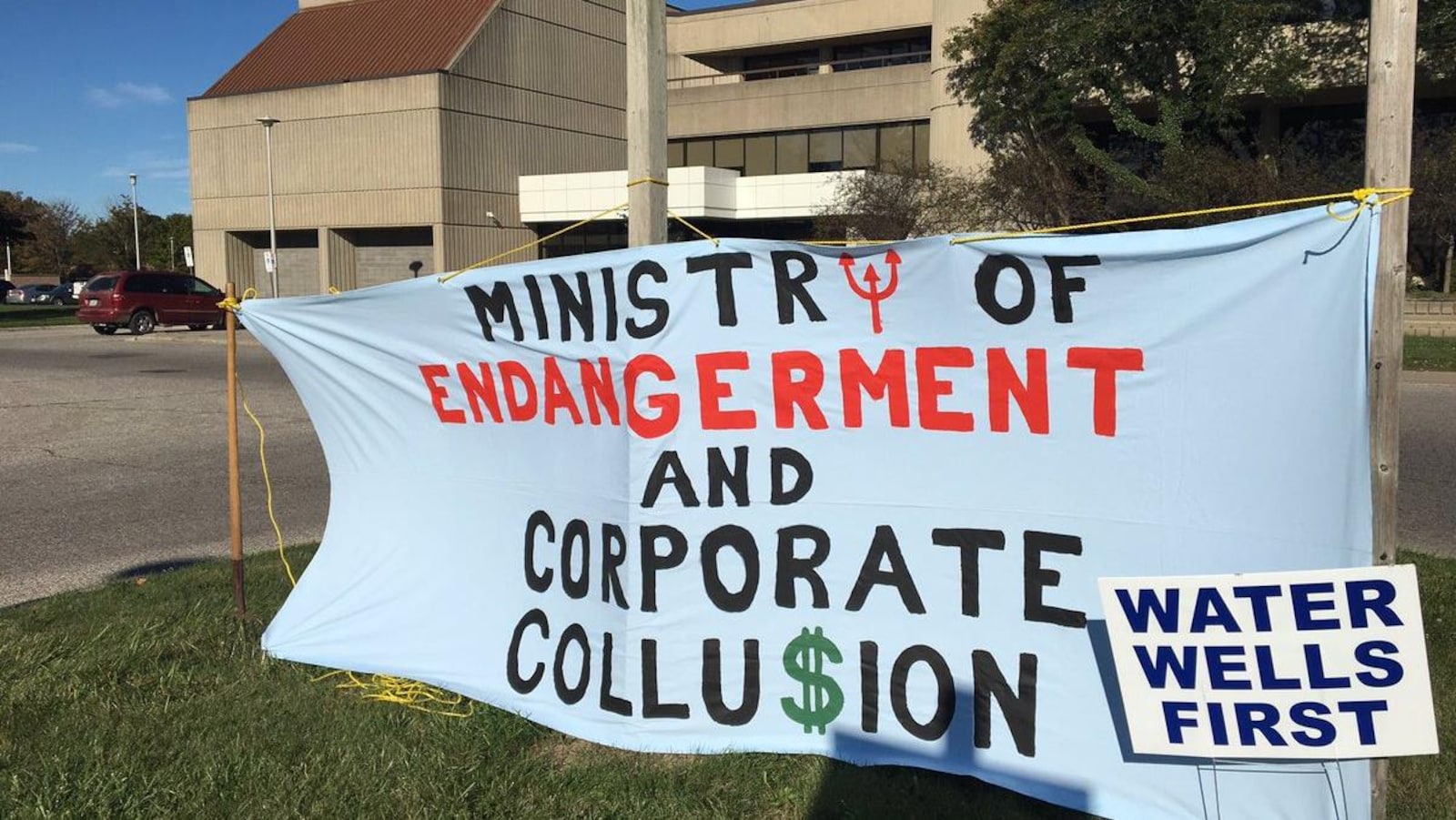 Vue extérieure d'un palais de justice. Une banderole dit : «Ministry of endangerment and Corporate Collu$ion» est installée sur une pelouse devant