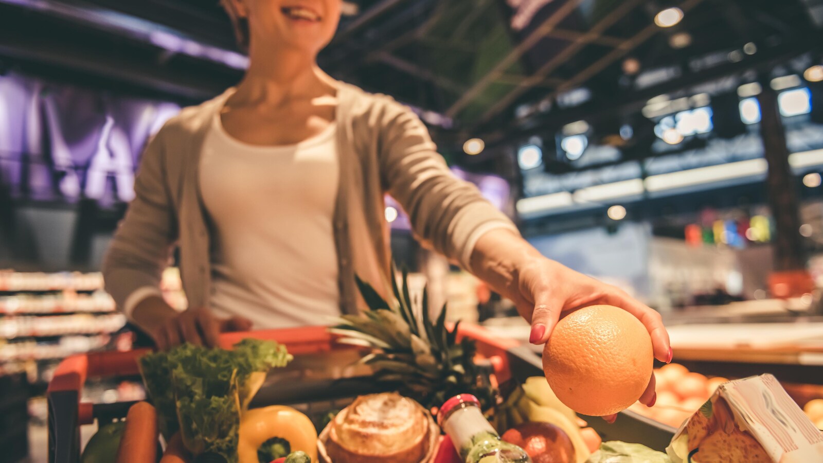 Une femme pousse un panier d'épicerie rempli de légumes et de fruits.