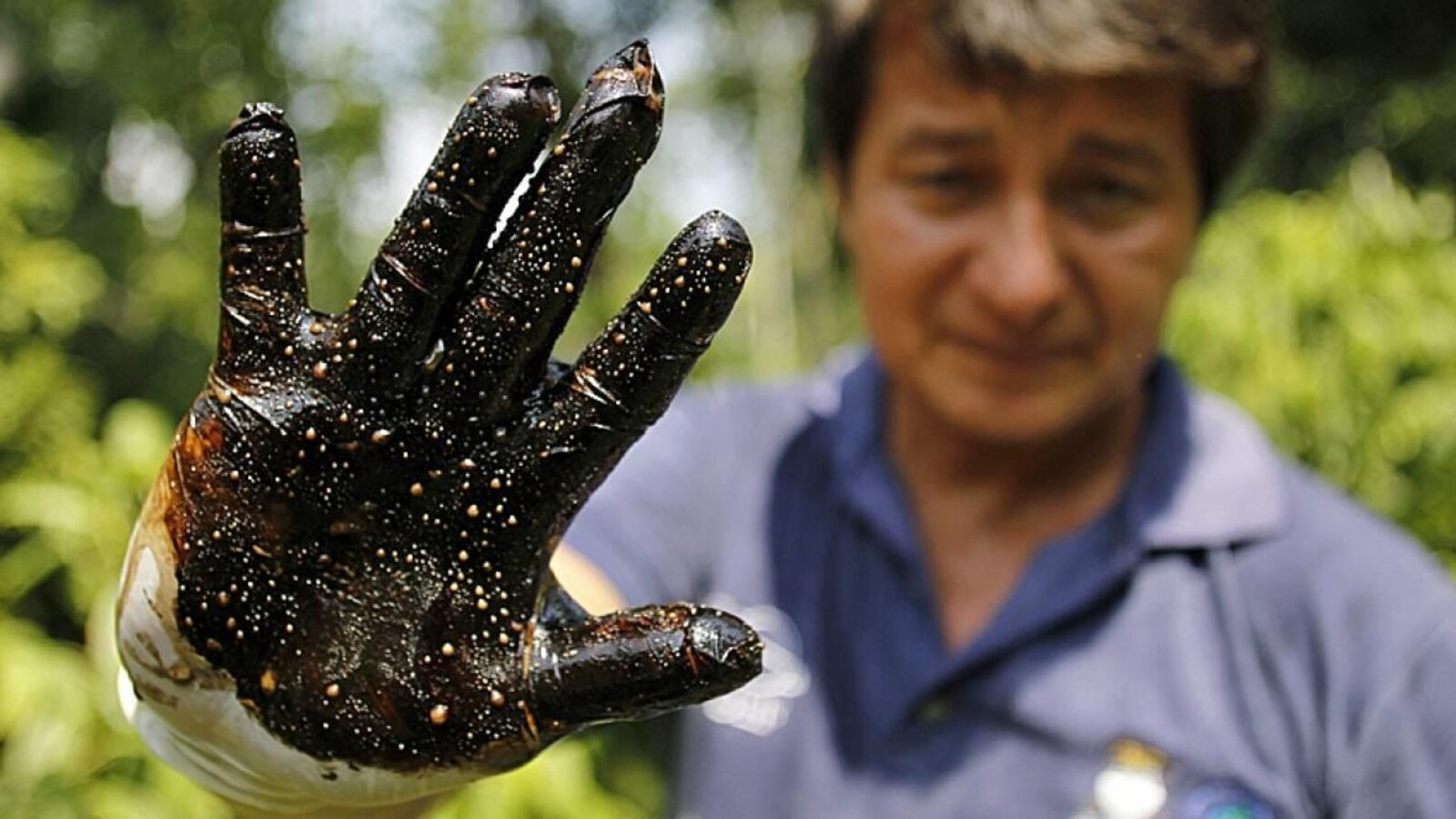 Un homme montre sa main couverte de pétrole brut.