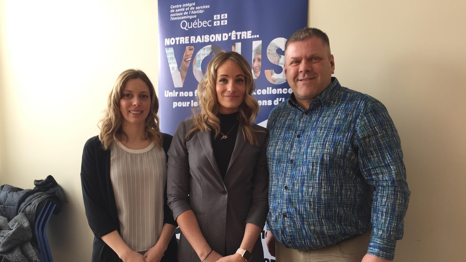 Deux femmes et un homme posent devant une affiche du Centre intégré de santé et de services sociaux de l'Abitibi-Témiscamingue.