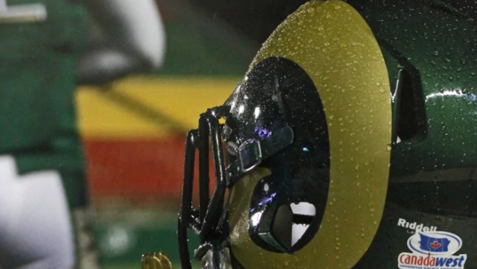 Un casque de footbal doré et vert vu de près avec un arrière-plan flou qui ressemble à un terrain de football.