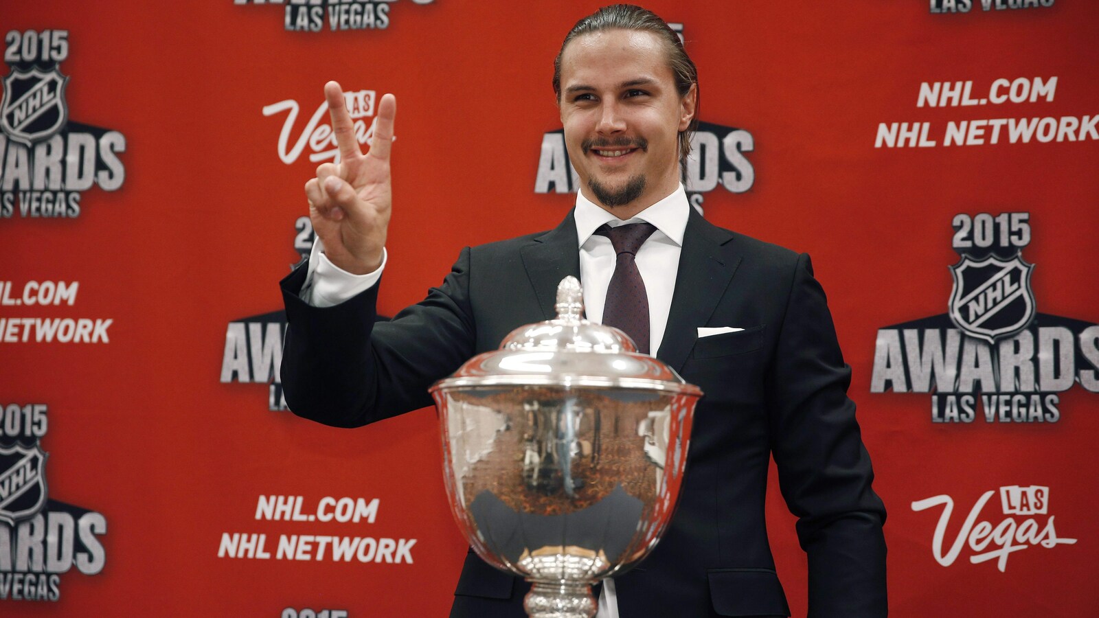 Erik Karlsson salue les caméras en se tenant derrière un trophée.