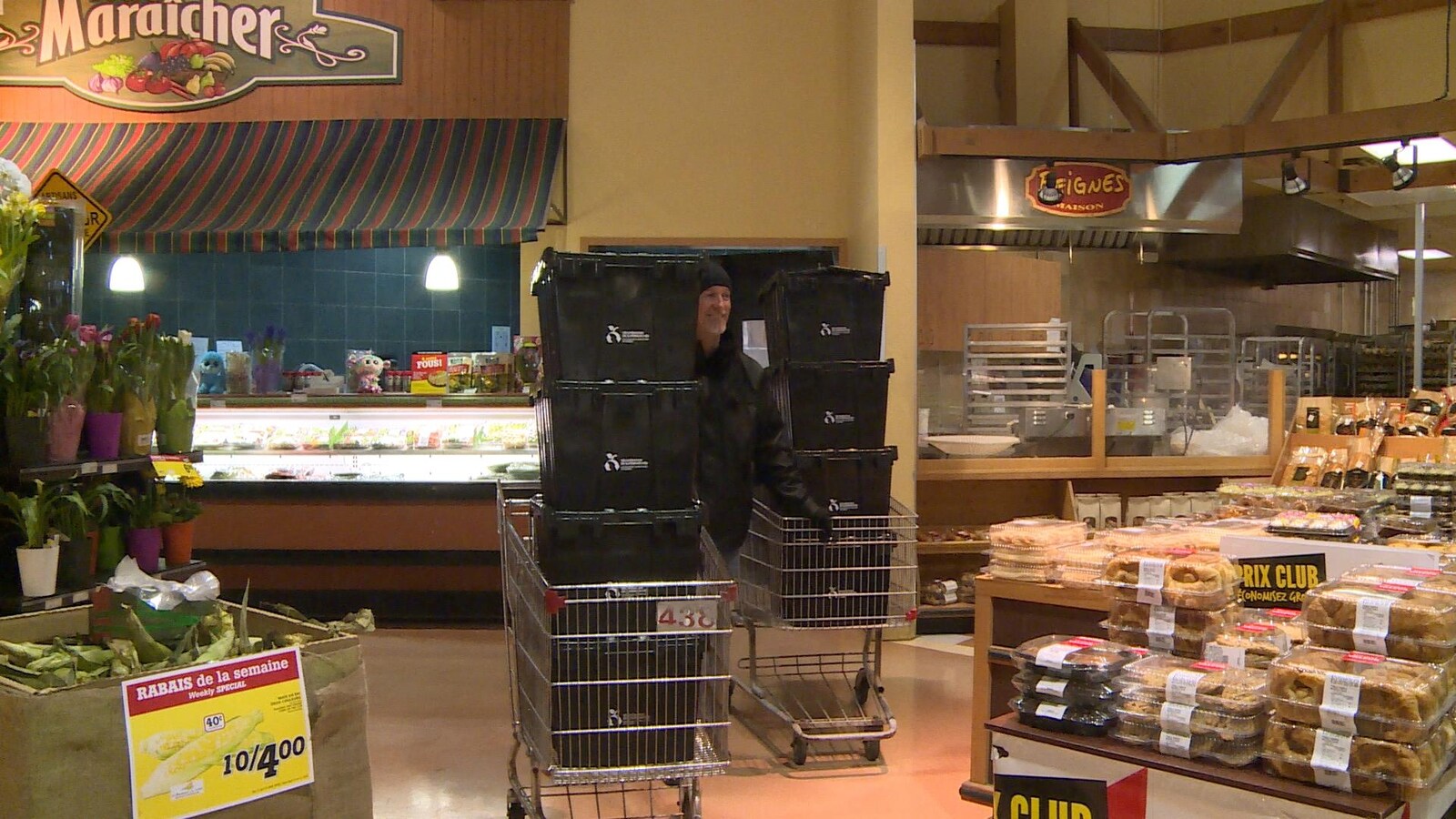 Un homme entre deux paniers d'épiceries remplis de caisses noires dans un supermarché.
