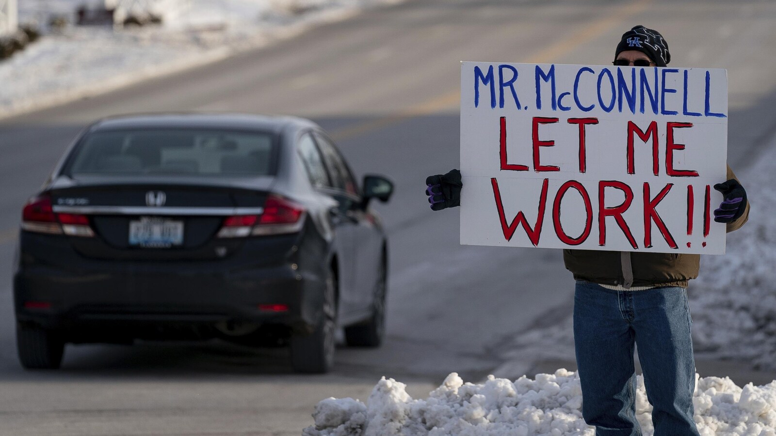 Un homme tient une affiche devant les bureaux du sénateur américain Mitch McConnell, à Park Hills, dans le Kentucky, le mardi 22 janvier 2019.