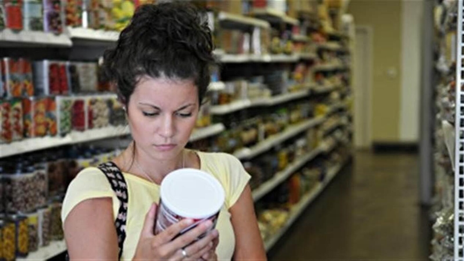 Une femme examine l'étiquette d'une conserve dans une épicerie.