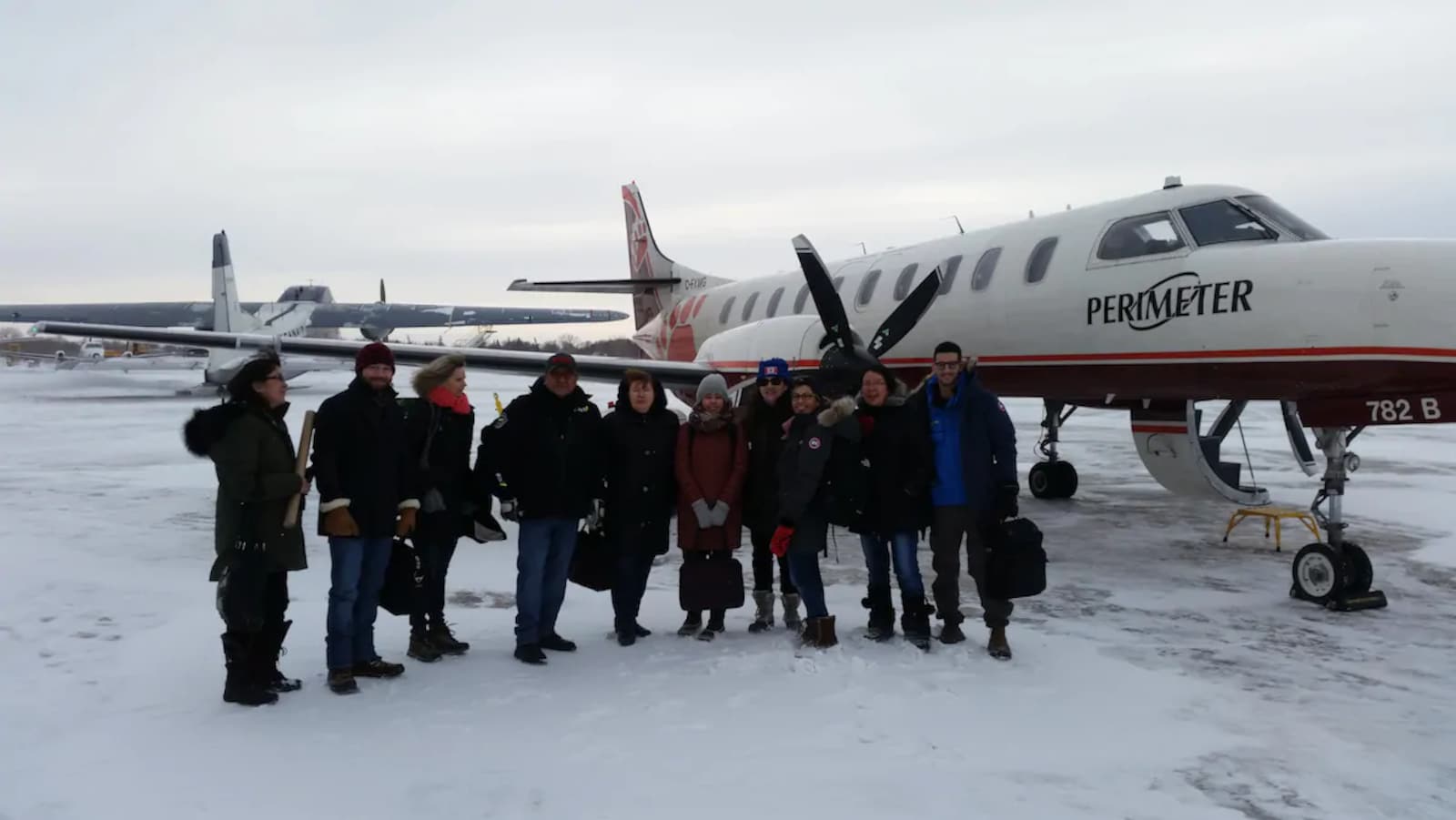Dix professionnels de la santé avec des manteaux d'hiver devant un petit avion.