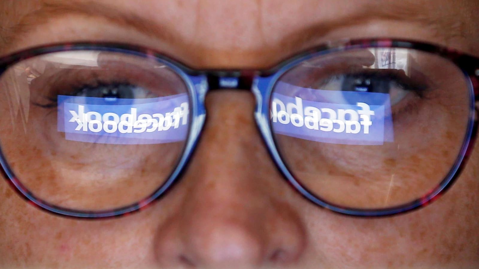 Le logo de Facebook se reflète dans les lunettes d'un homme qui regarde un écran.