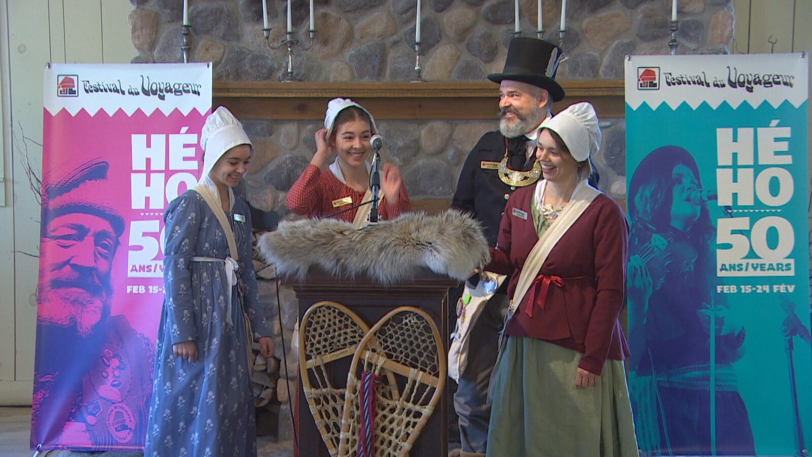 La famille de voyageurs, dans leurs costumes traditionnels, souriants, devant une estrade. En arrière, des bannières indiquent « Hé Ho, 50 ans ».