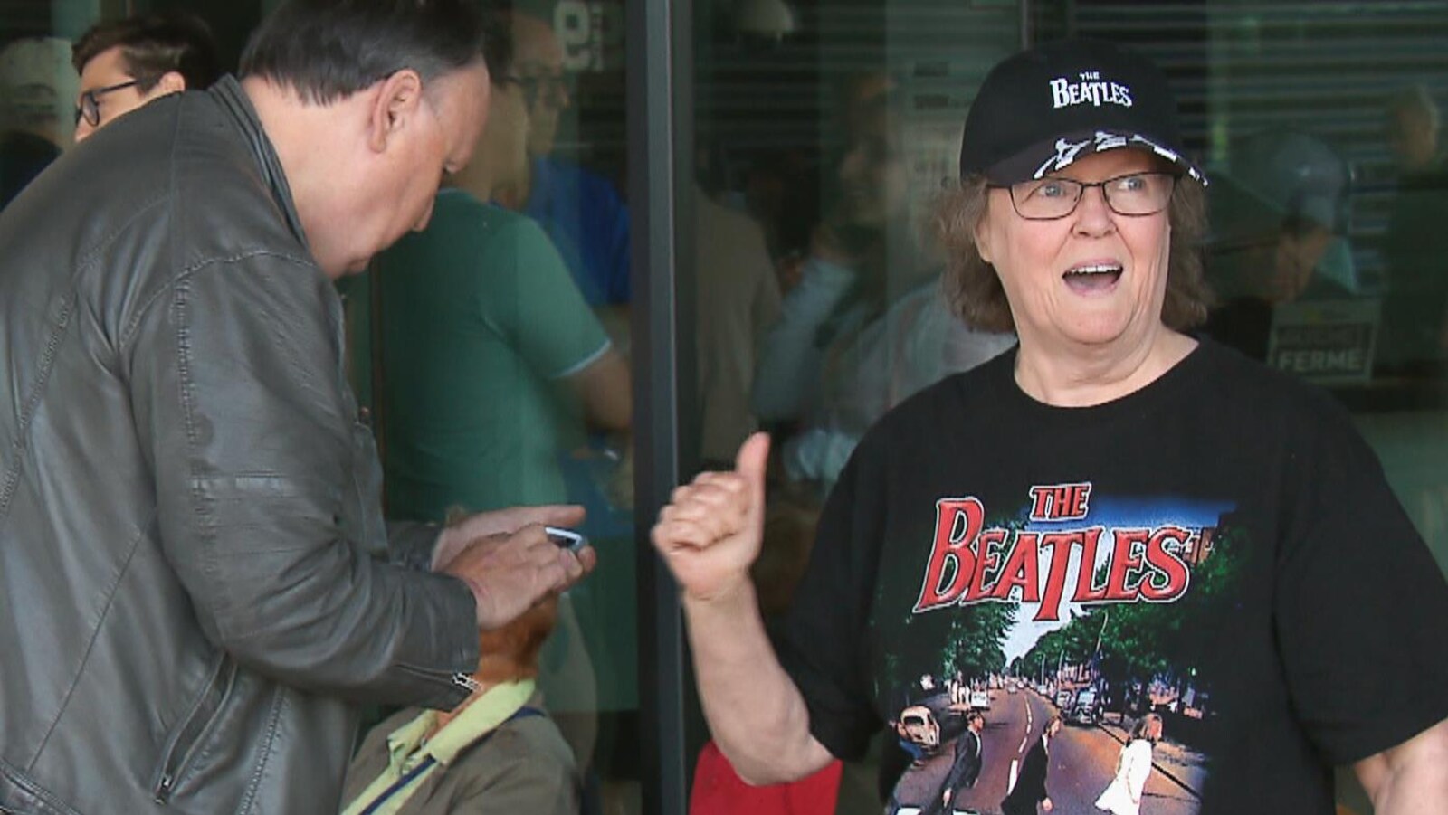 Une fan portant un chandail des Beatles fait un signe de pousse en l'air en attendant son tour dans la file.