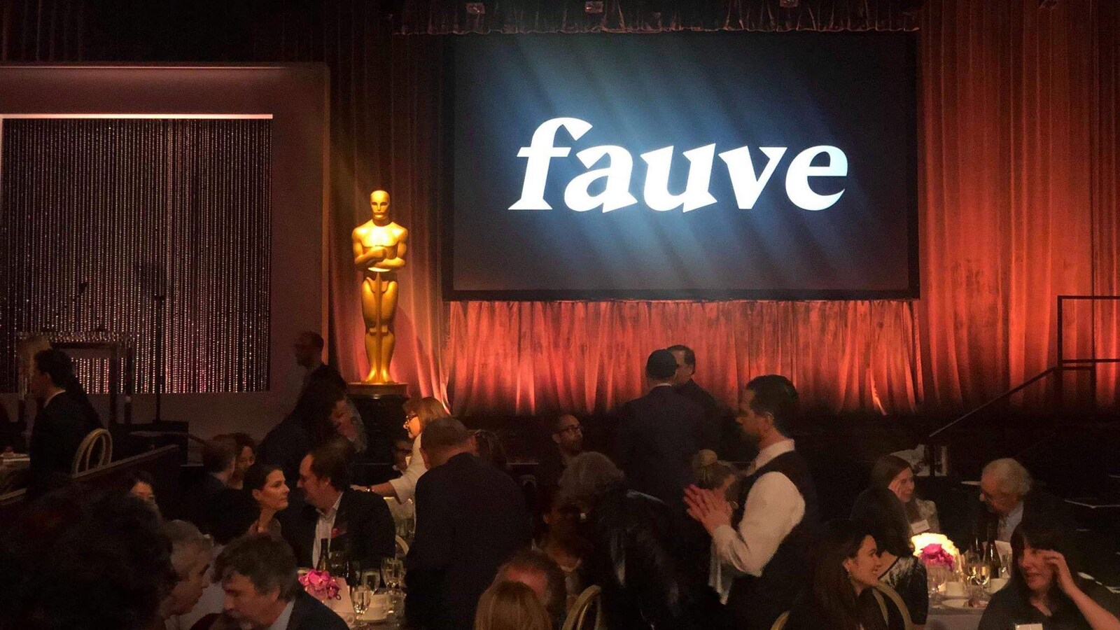 Un écran de cinéma sur lequel est écrit Fauve dans une salle où des personnes sont attablées.