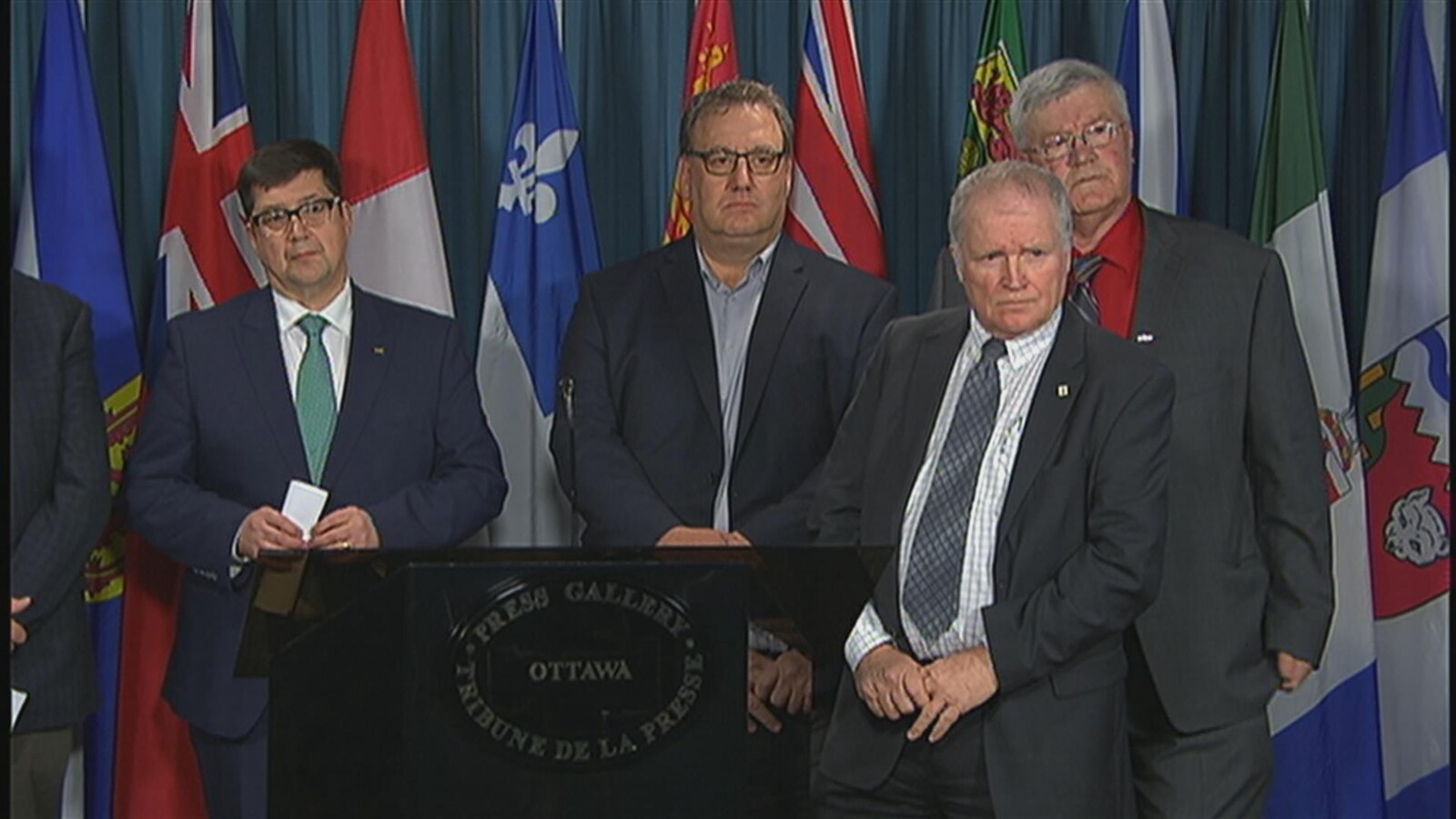 Quatre directeurs et présidents d'organisations vouées à l'agriculture sont debouts devant des drapeaux des provinces.