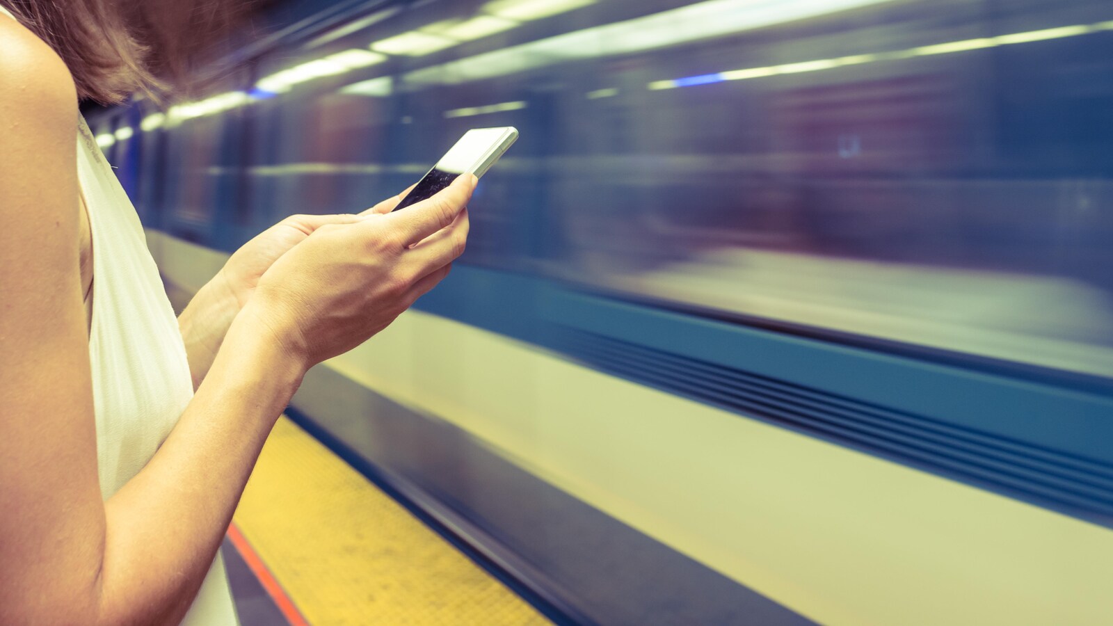 Une femme utilise un cellulaire sur un quai du métro de Montréal.