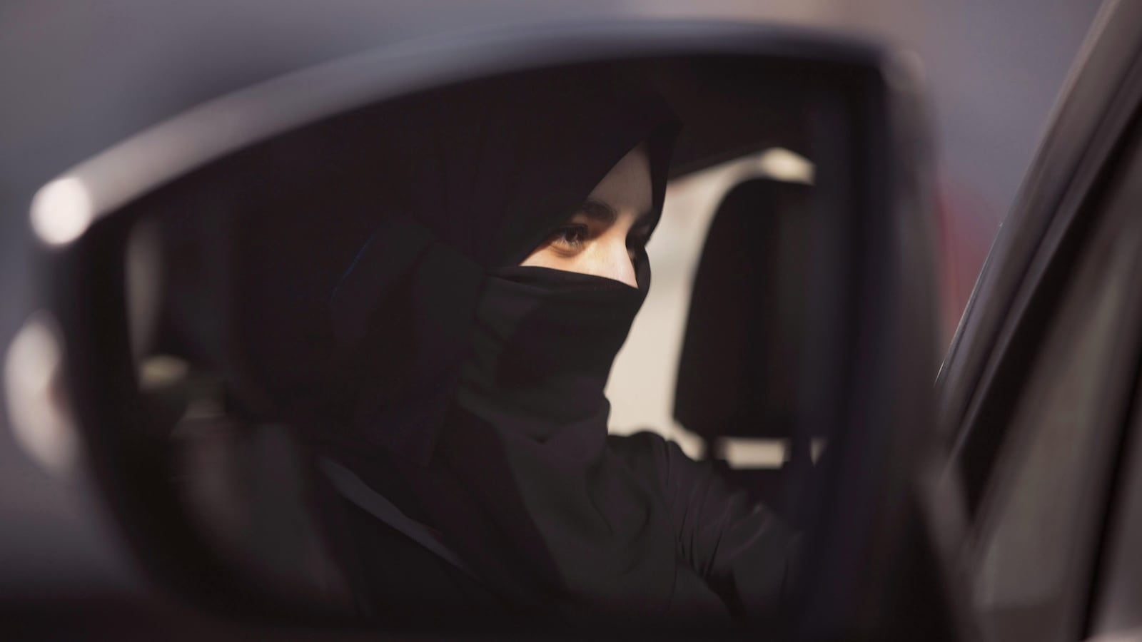 Dans un rétroviseur, le visage d'une femme au volant d'une voiture.