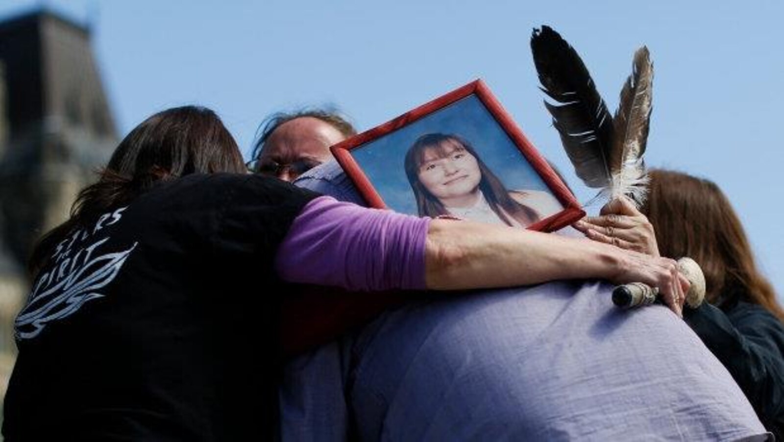 Quatre personnes se serrent dans les bras en portant la photo d'une femme.