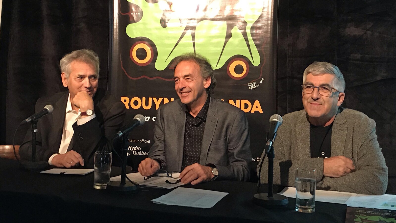 Trois hommes sont assis derrière une table durant une conférence de presse.