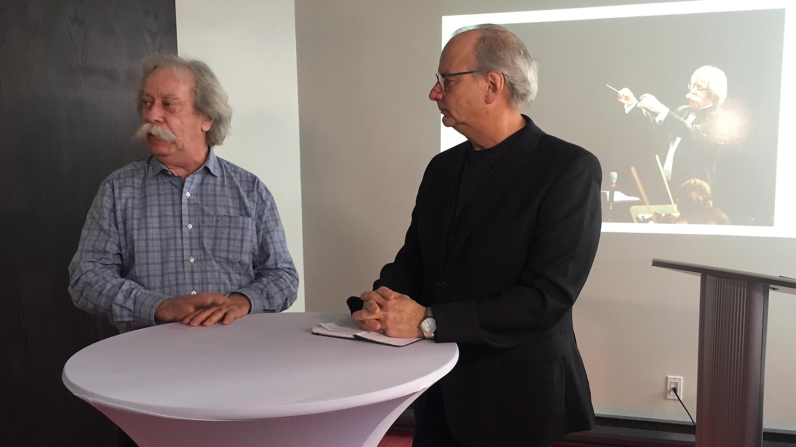 Deux hommes sont accoudés à une table haute lors d'une présentation.