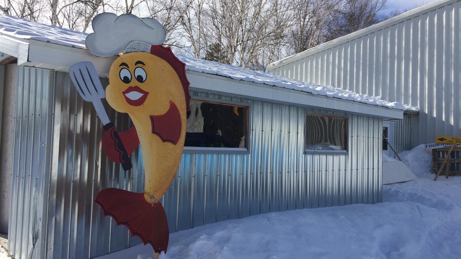 Un poisson avec une spatule et un chapeau de chef orne une cabane en tôle.
