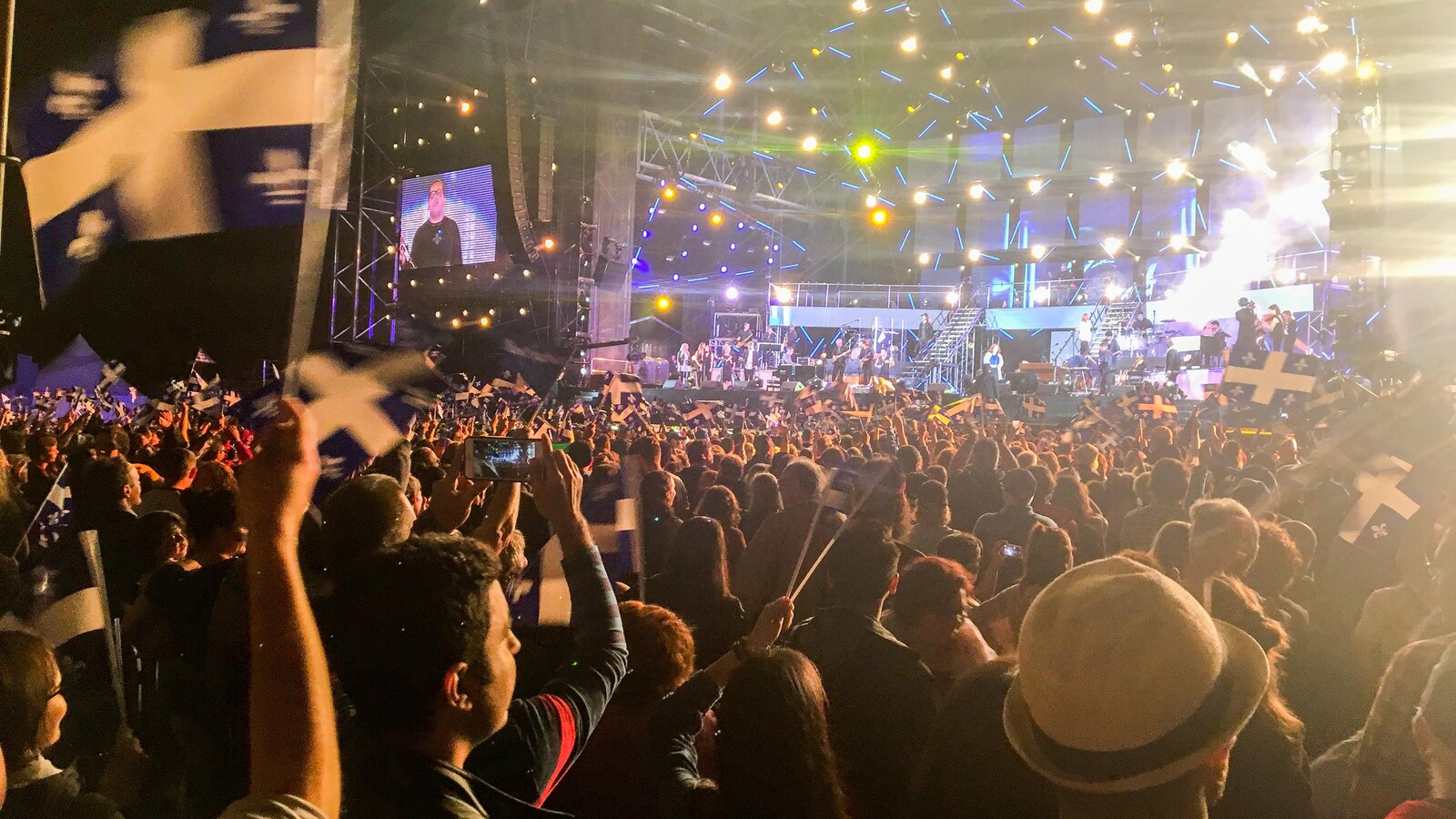 De nombreuses personnes, dont certaines avec un drapeau du Québec en main, assistent à un spectacle extérieur le soir.