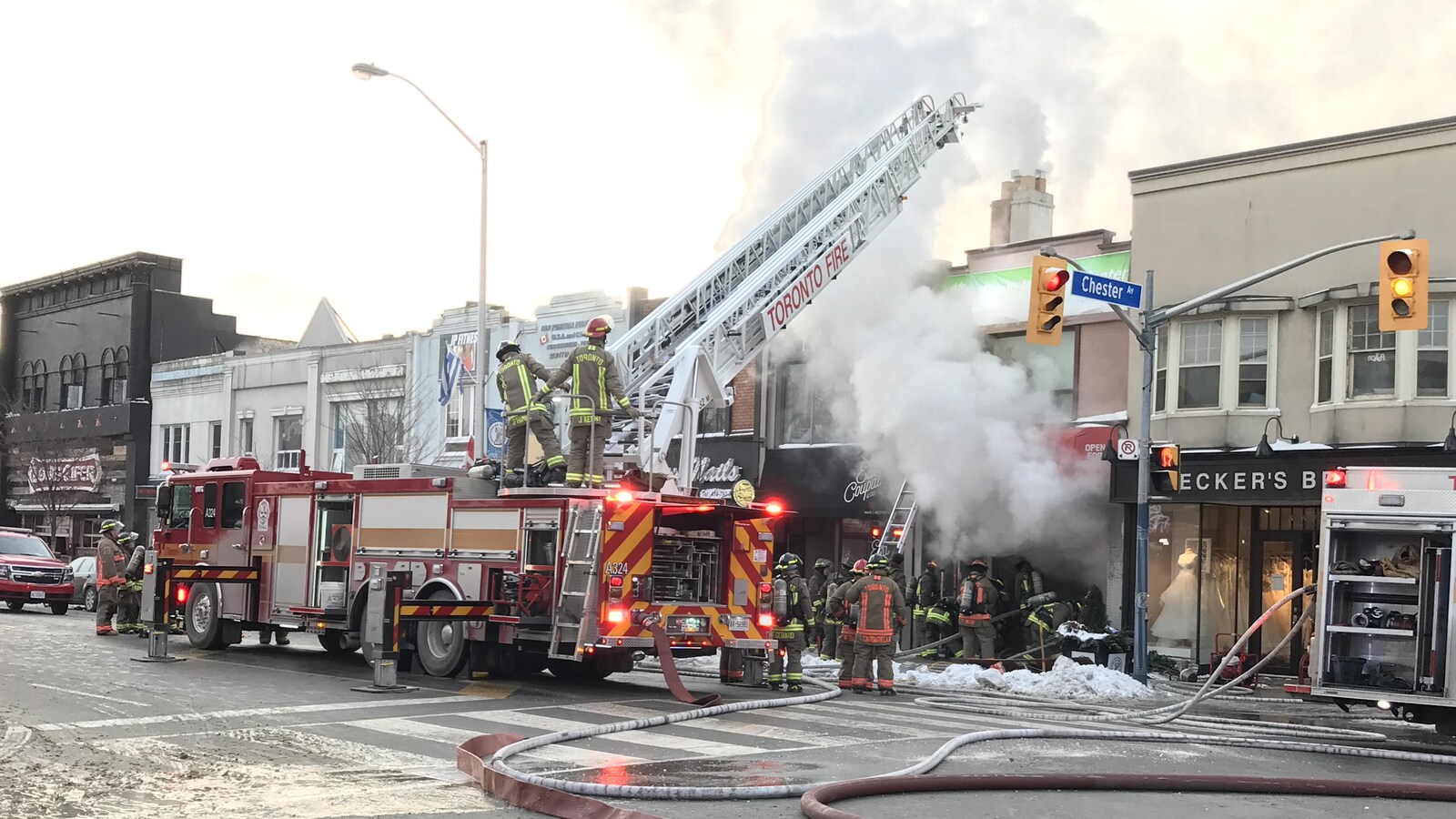 Photo d'un camion de pompier, l'échelle est déployée; des pompiers sont devant un commerce d'où s'échappe de la fumée.