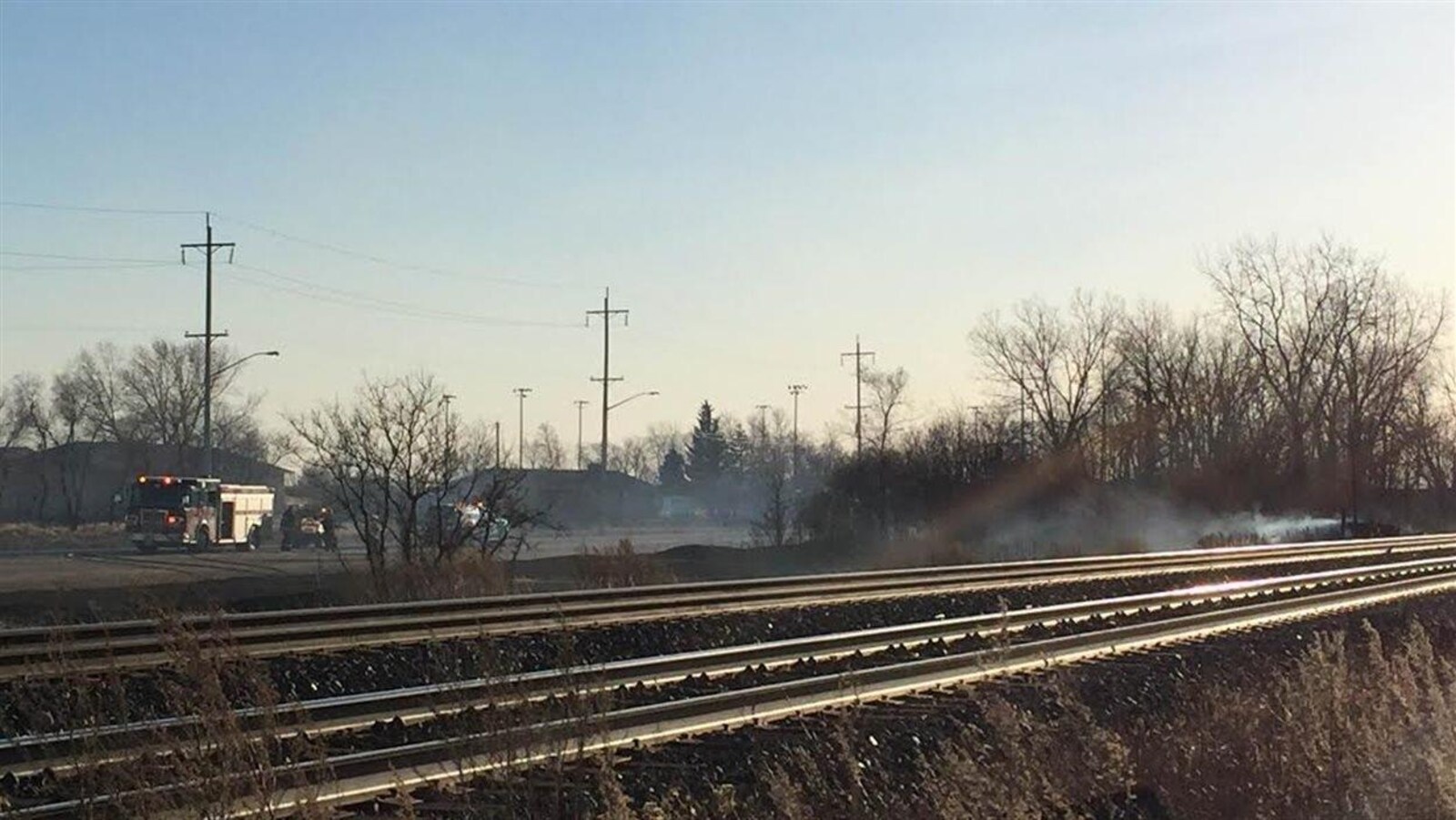 Des pompiers éteignent un feu près de la voie ferrée.
