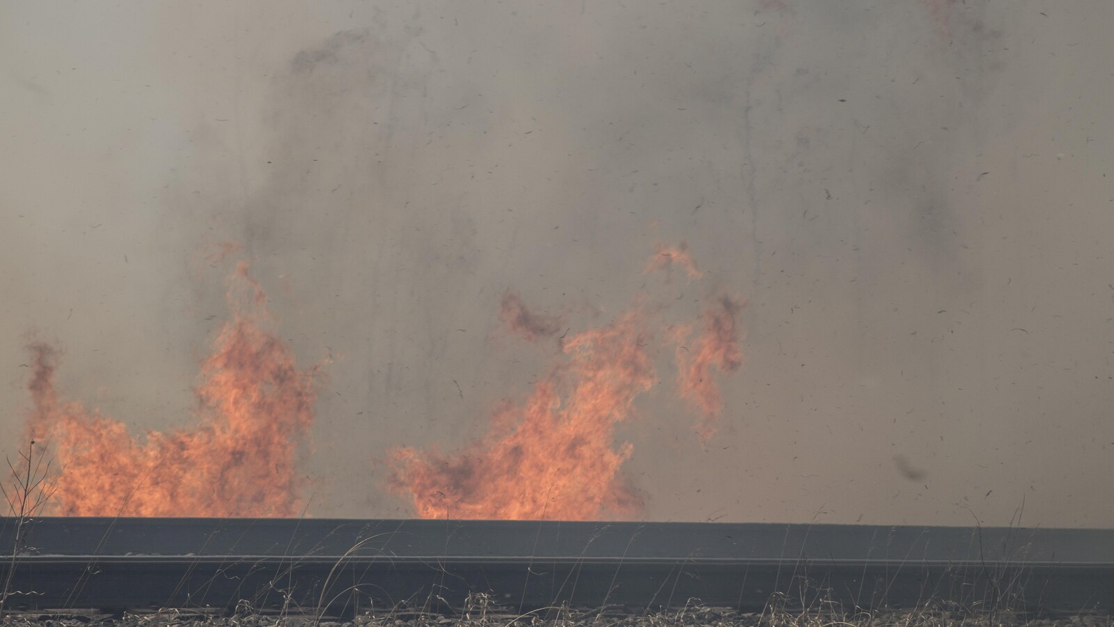 En avant-plan, une voie ferrée, en arrière-plan des flammes et de la fumée.