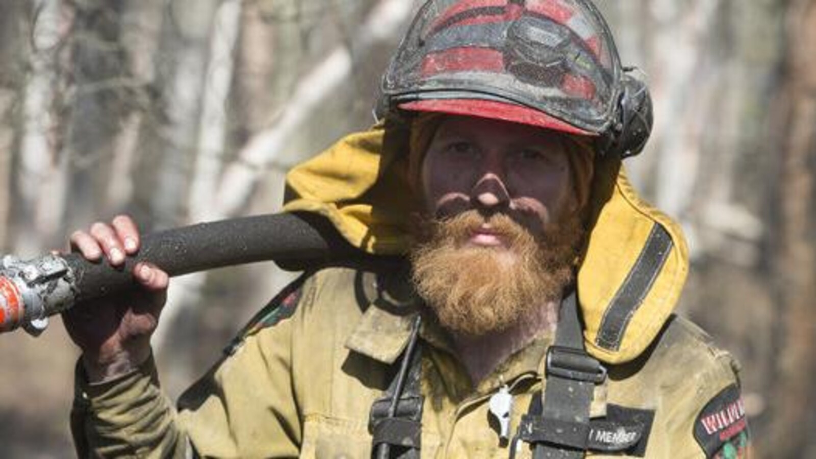 Un pompier forestier qui vient de combattre un feu. Il porte l'habit jaune des pompiers et il a le visage plein de suie.