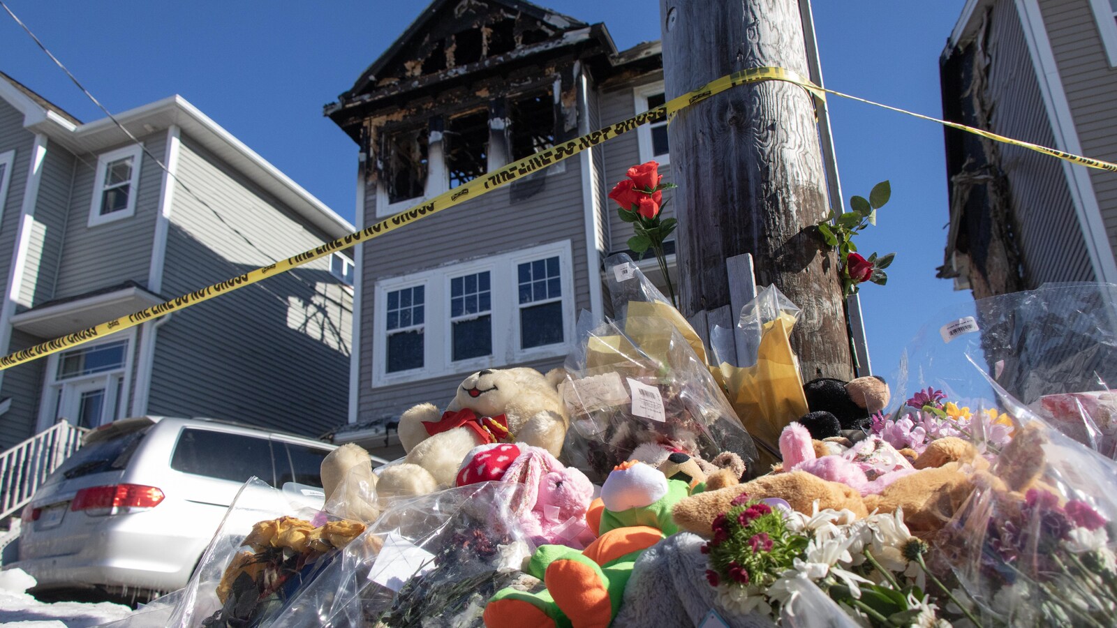 Des oursons en peluche et des fleurs devant la maison, ravagée par les flammes.