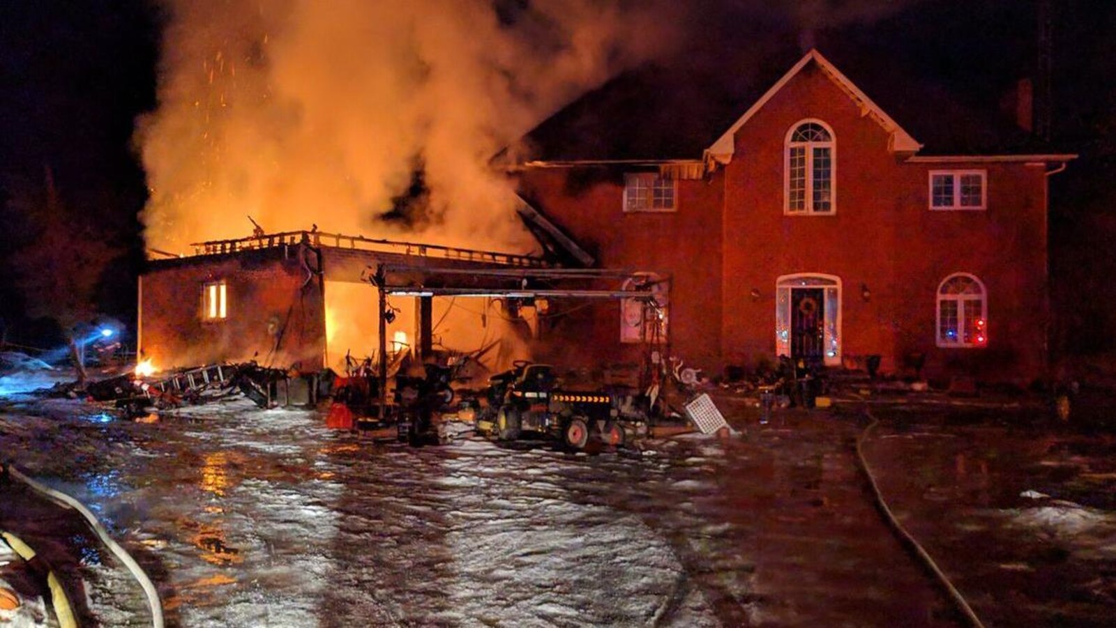 Le garage d'une grande maison en feu en hiver durant une intervention des pompiers.