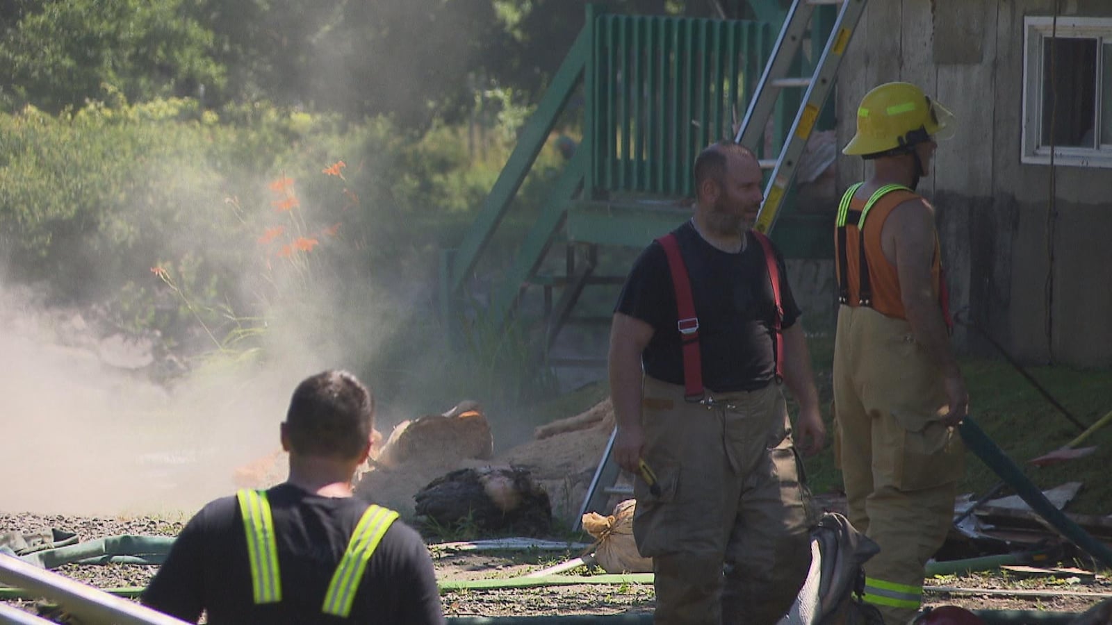 Trois pompiers marchent à proximité d'une maison et de la fumée.
