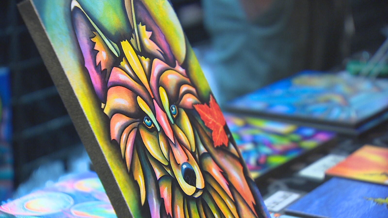 Une peinture d'un loup multicolore en avant-plan avec d'autres oeuvres d'art en arrière-plan.