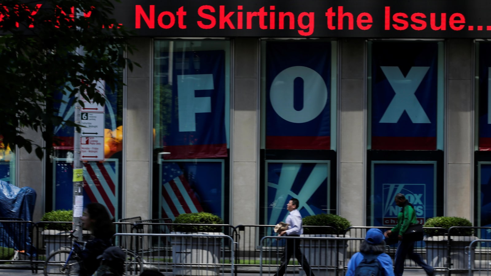 Des passants circulent devant un immeuble sur lequel on peut voir des publicités de Fox News.