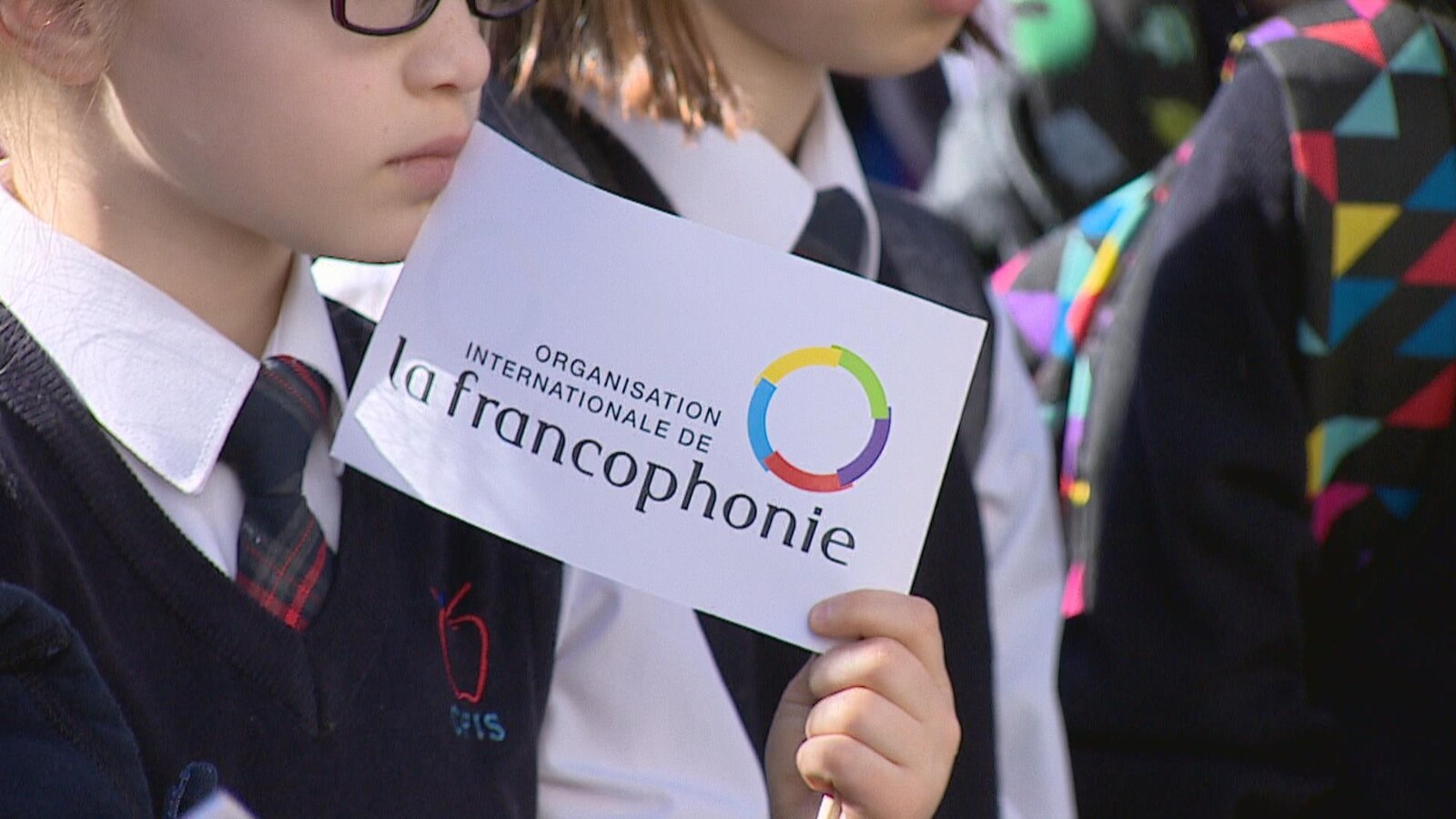 Vue sur une jeune fille qui porte des lunettes. Elle tient dans ses mains un drapeau où il est écrit: organisation internationale de la francophonie.