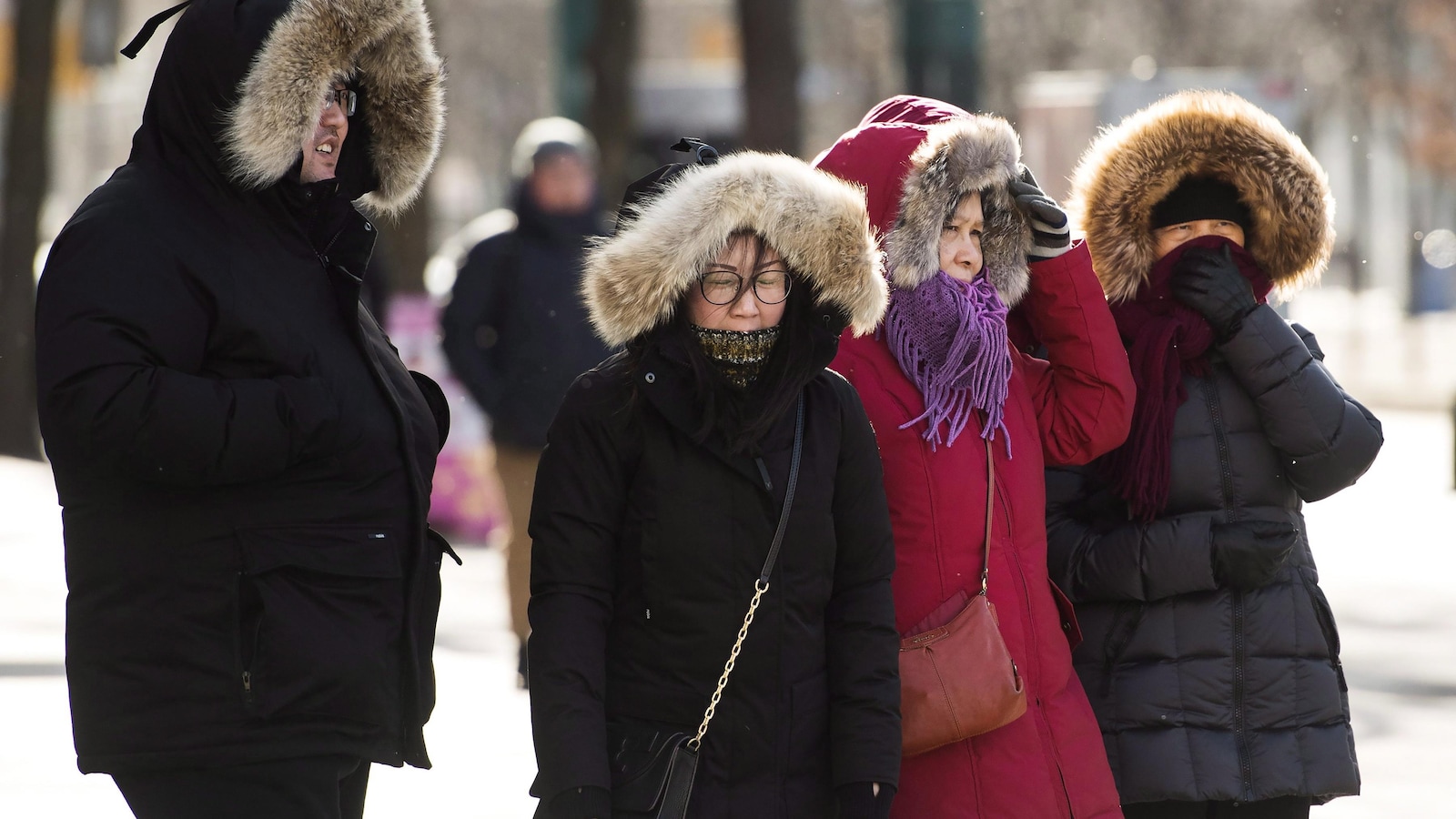 Trois femmes et un homme qui grelottent dehors au coin d'une rue, malgré leur gros manteau d'hiver.