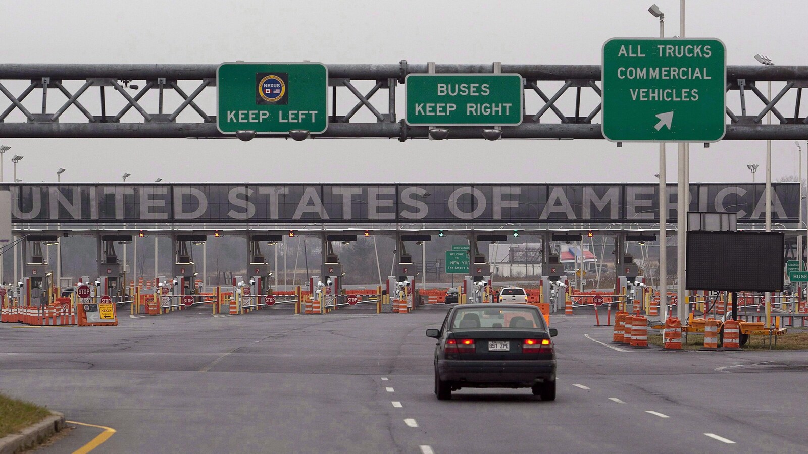 Une voiture s'approche d'un gros poste douanier. On voit l'indication ''United States of America'' en gros au-dessus les pancartes.