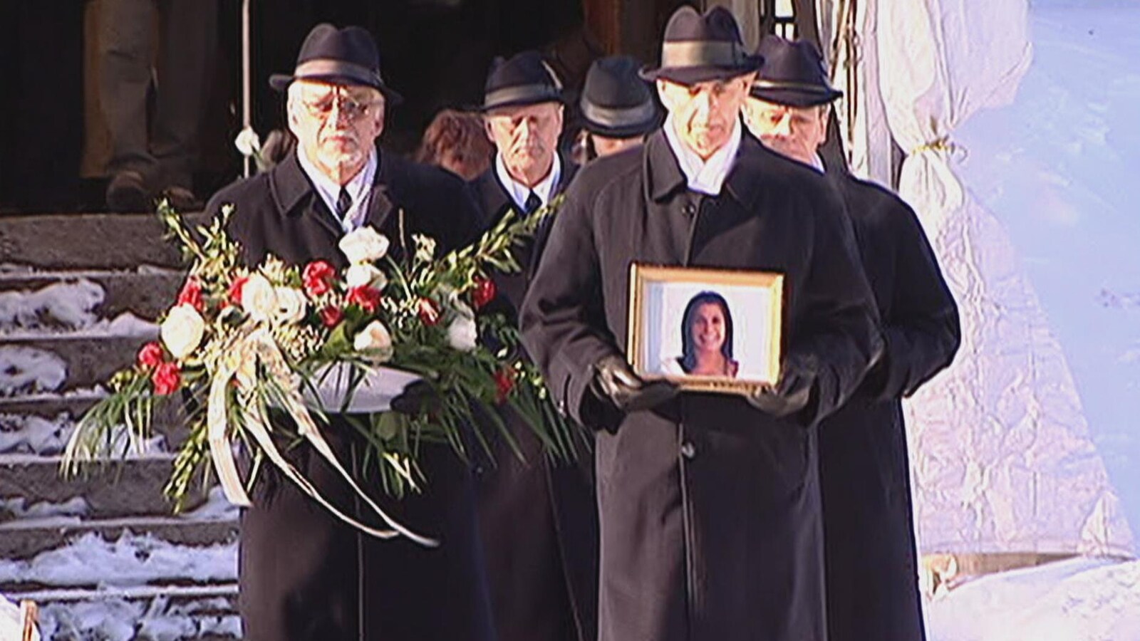 Des hommes transportant une gerbe de fleurs et une photo de Mélissa Lambert sortent de l'église.