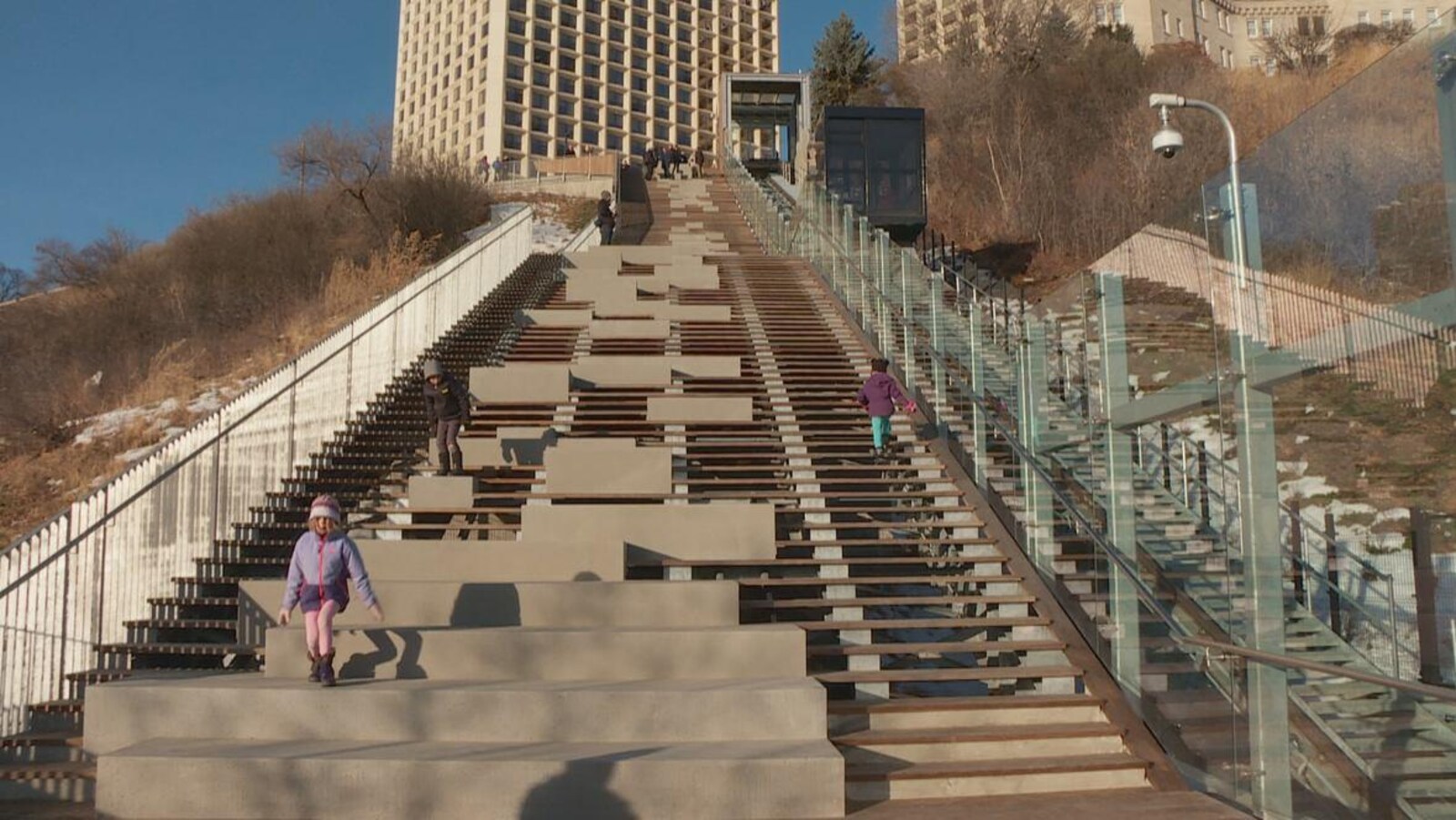 Le funiculaire fonctionne pendant que des enfants montent et descendent un escalier qui se trouve à ses côtés.