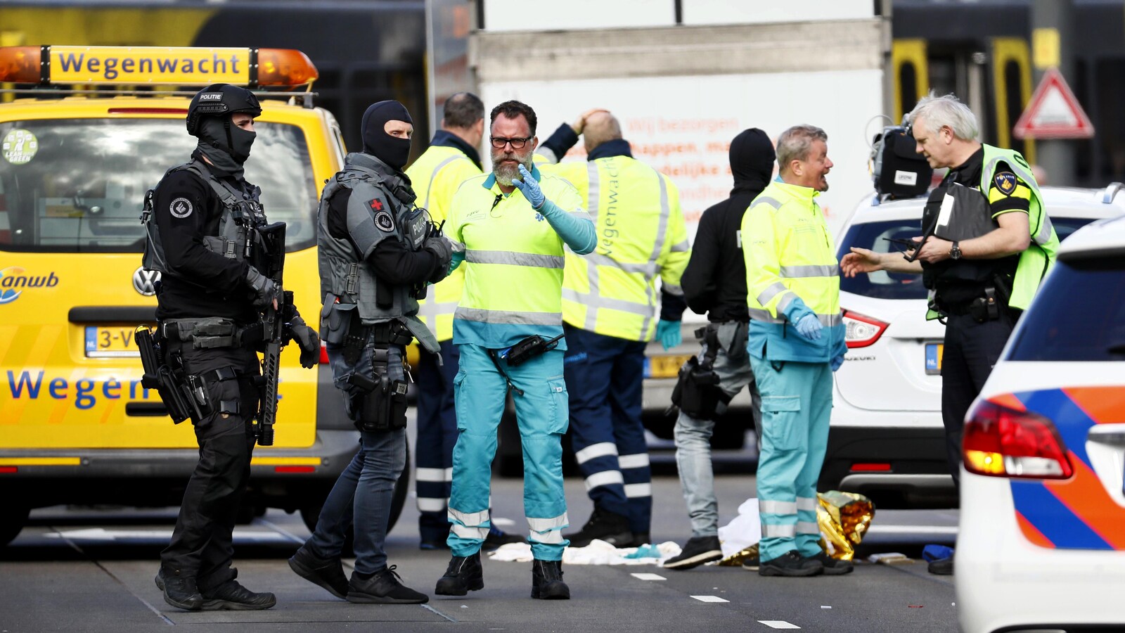 Les forces de l'ordre, cagoulées et armées, discutent avec les services d'urgence, en vêtements d'intervention jaune fluo.