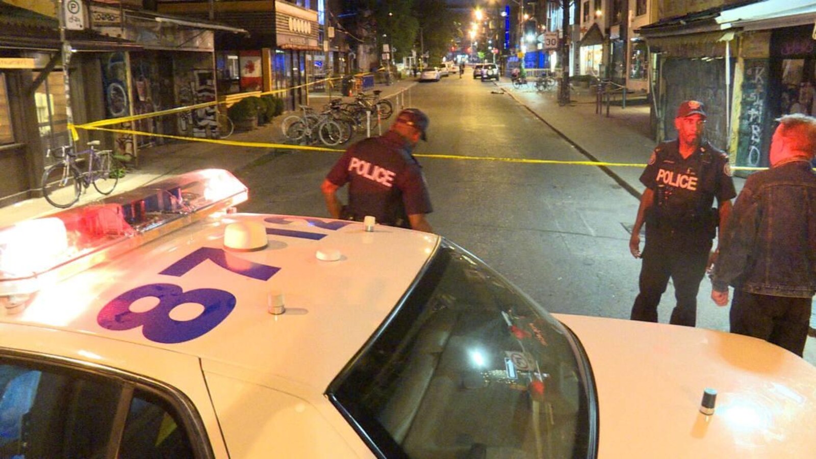 Photo d'une autopatrouille, d'une banderole jaune et de policiers bloquant une rue.