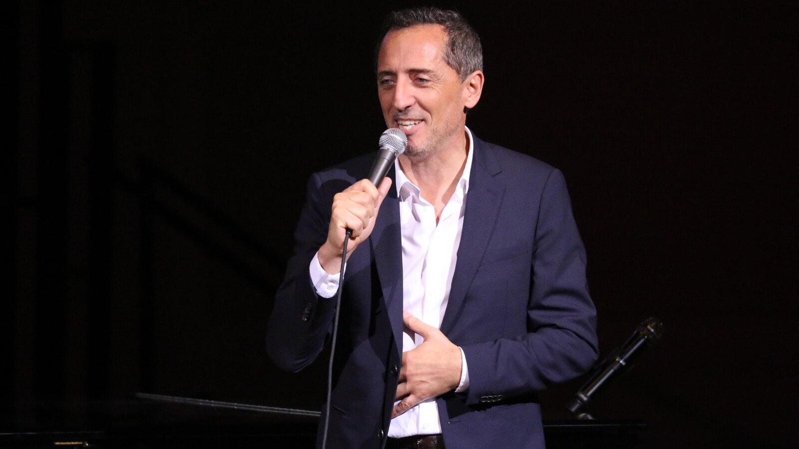 L'homme est sur une scène avec un micro et sourit.
