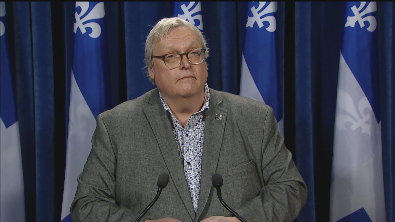 Gaétan Barrette lors d'un point de presse à l'Assemblée nationale avec des drapeaux du Québec en arrière fond