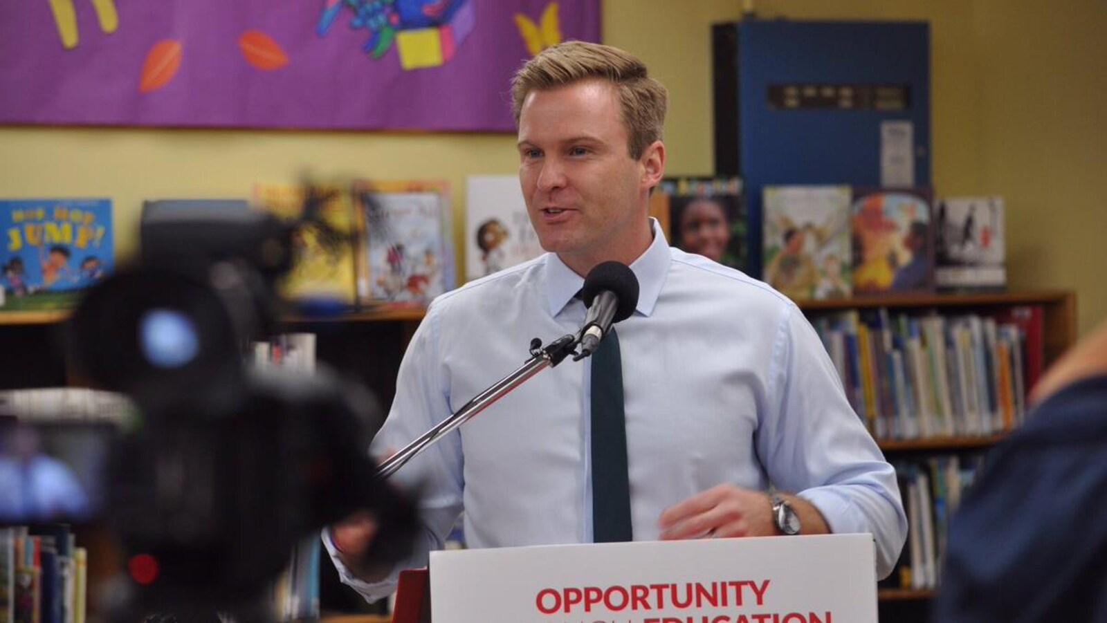 Brian Gallant donne une conférence de presse dans la section des livres pour enfants d'une bibliothèque publique.