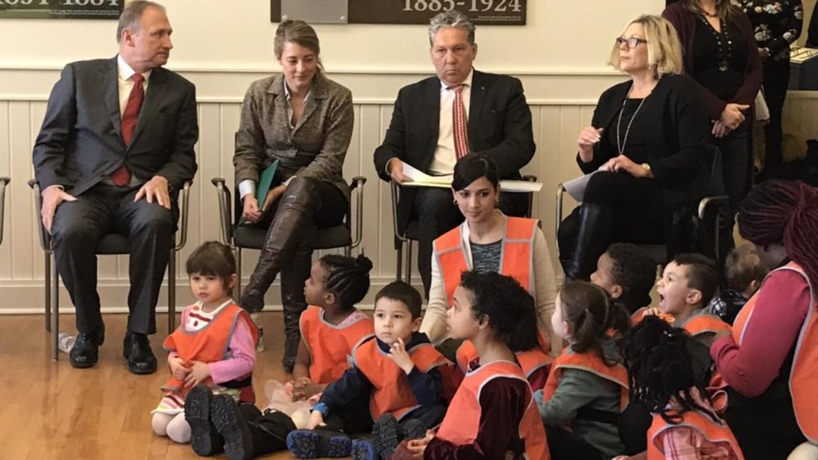 Quatre adulte sont assis sur des chaises, avec des enfants d'une garderie assis par terre devant eux.