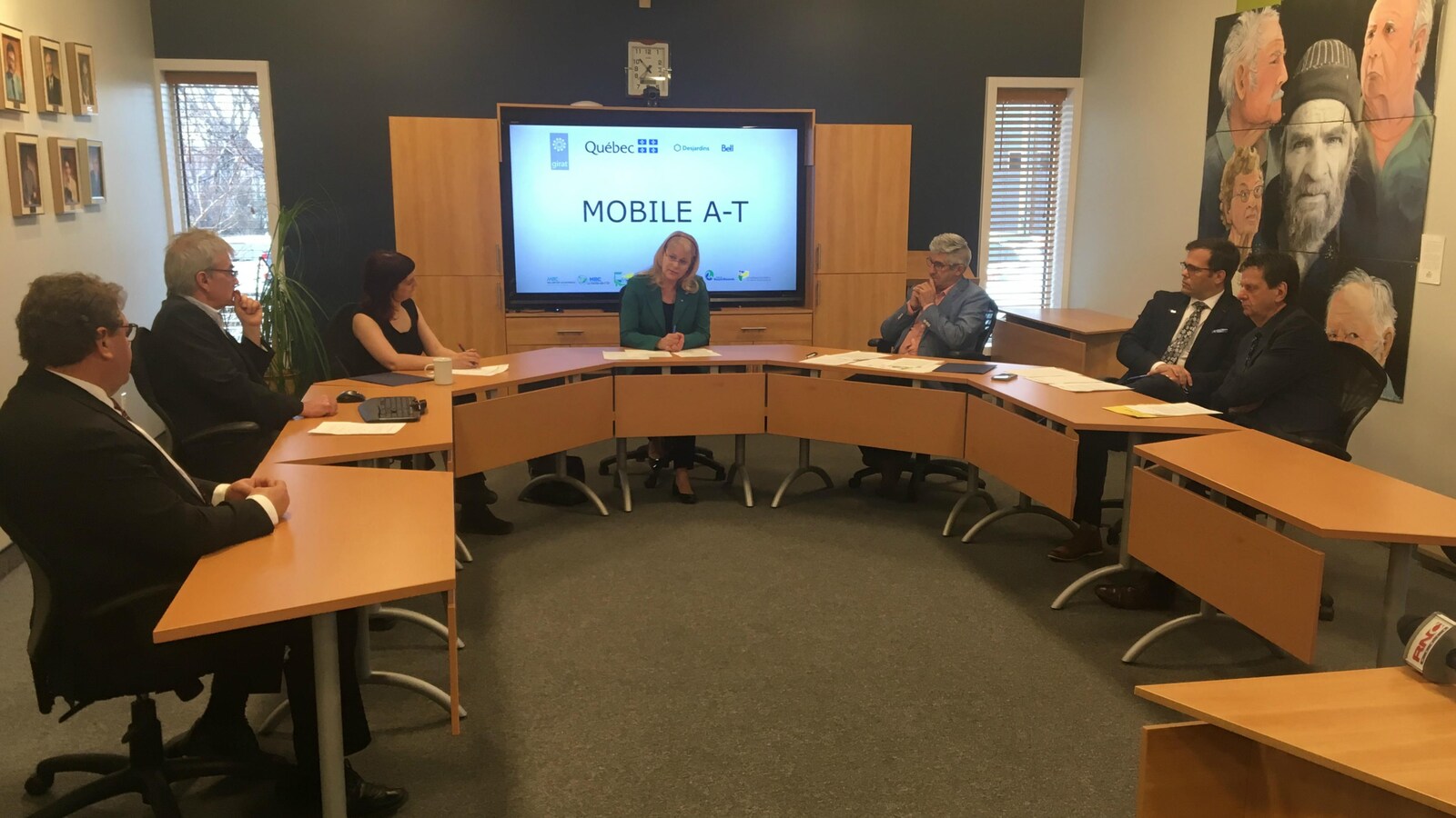 Des hommes et des femmes sont assis derrière une table de salle de conférence lors d'une présentation nommée Mobile A-T.