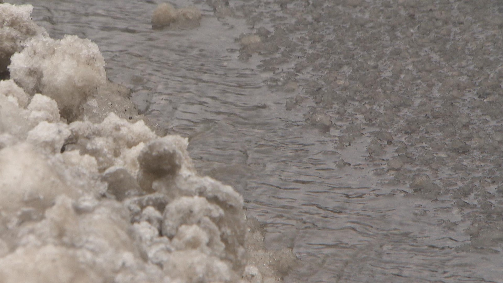 Un amas de neige juxtaposé sur de l'eau qui ruisselle en bordure de rue.
