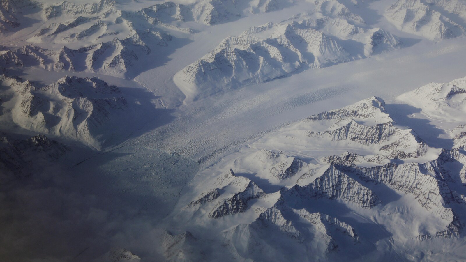 Des montagnes, toutes enneigées, sont photographiées des airs. Elles sont parfois séparées par une bande de glace.