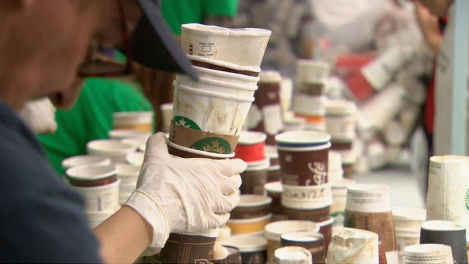 Une main gantée tient une pile de contenants en carton et on vous aussi plusieurs contenants similaires empilés en arrière-plan